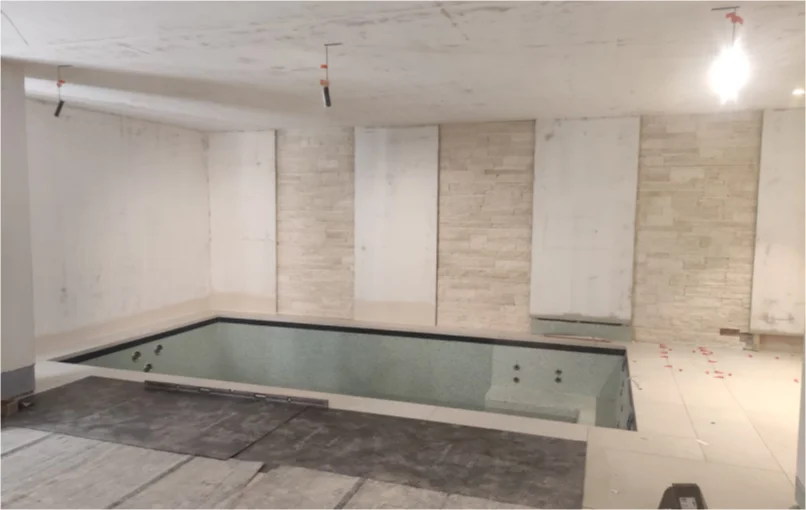 This image depicts the swimming pool in the basement with light grey stone wall accents/partitions.